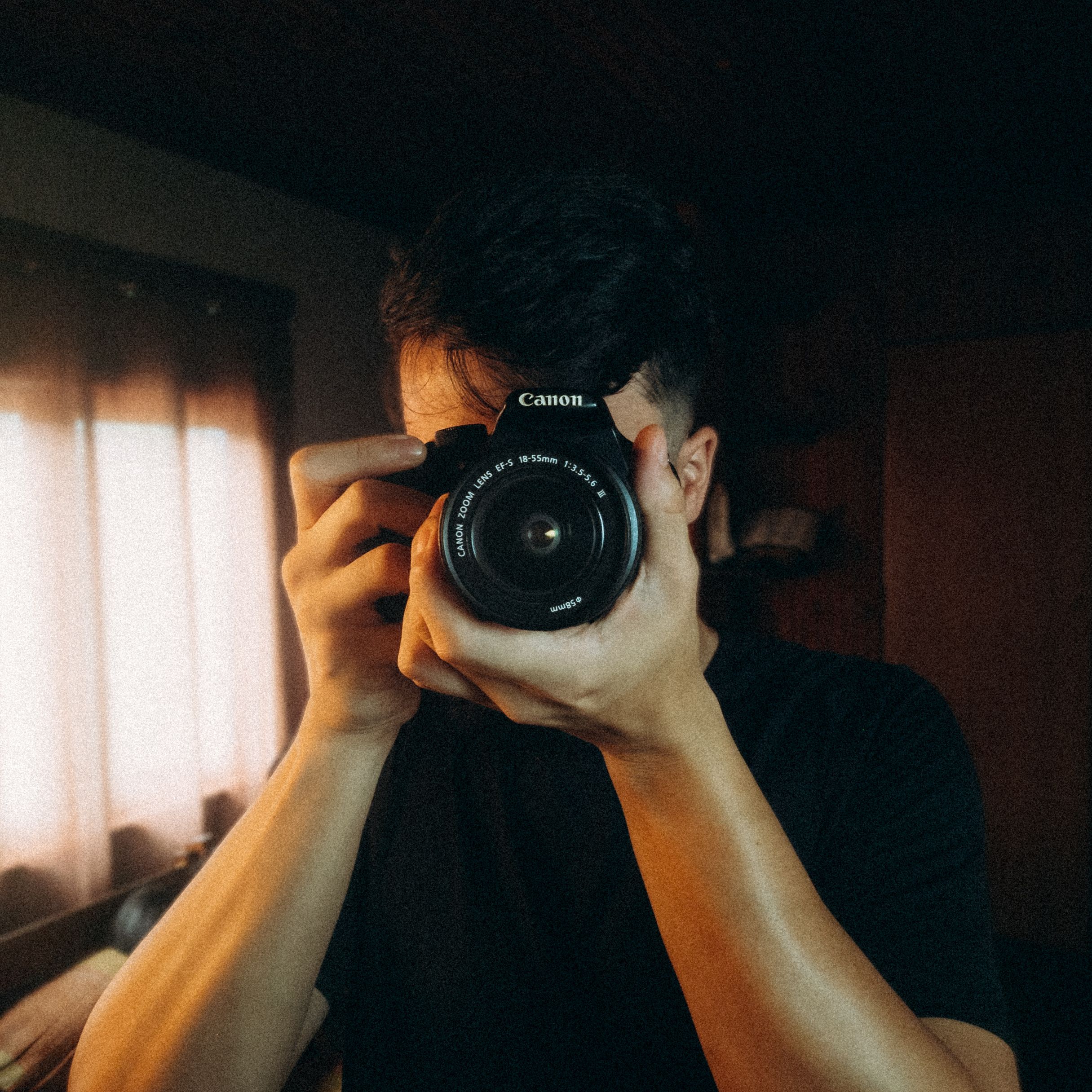 A young man taking a photo indoors with a DSLR camera, showcasing creative photography.